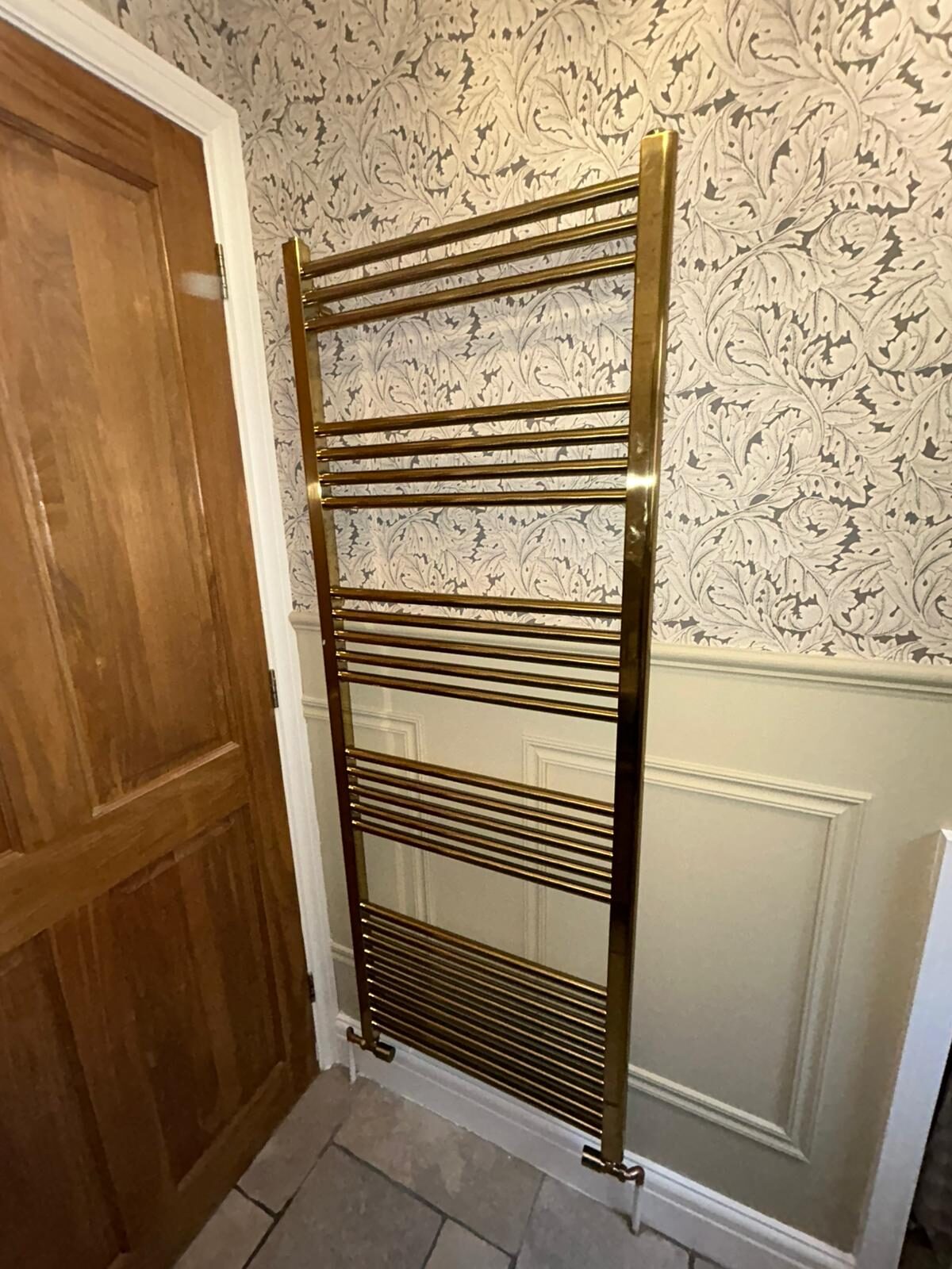 Heritage brushed-brass heated towel rail installed against William Morris wallpaper — luxury bathroom heating